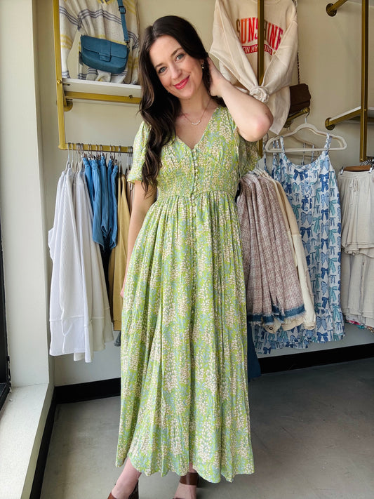 Introducing our Fern Smocked Waist Button Dress, a playful revamp on our best-selling design! Made with a soft floral rayon fabric, this maxi dress features a flattering smocked waist, functional cover buttons, and elastic exaggerated sleeves. With raglan sleeves, a v neckline, and side pockets, this dress offers both style and convenience.