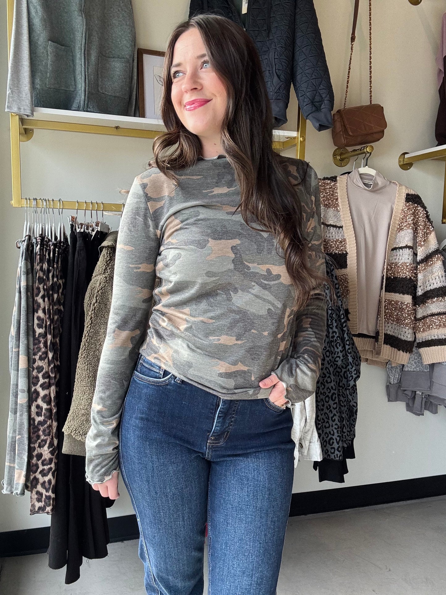 Add a fun twist to your wardrobe with this Camo Frilled Merrow Hem Top. The playful camouflage print pairs perfectly with the delicate frilled hem, adding a touch of flirty movement to your look. Featuring a cozy mock neck and long sleeves, this knit top keeps you comfy while standing out with style. Perfect for layering or wearing on its own, it’s a fresh way to mix casual with cute.
