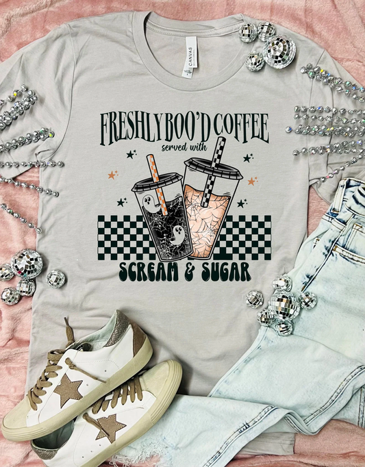 Gray t-shirt with coffee graphic and text, paired with sneakers and denim jacket on a pink background.