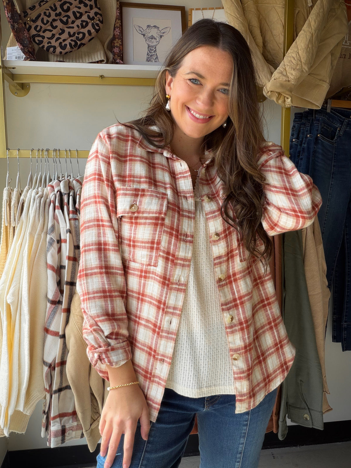 Model wearing a terracotta and ivory plaid button-up shirt open over an ivory top with jeans.