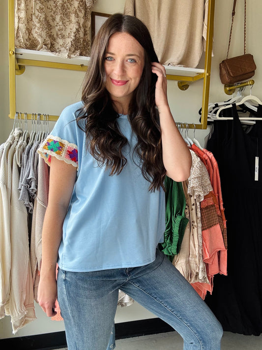 Crafted from lightweight French terry, the Light Blue Embroidered Sleeve Top offers both comfort and refined style. Its classic crew neck pairs seamlessly with batwing sleeves, which are accented by a delicate floral crochet detail at the edges. This subtle embellishment elevates the design, making it a versatile piece that combines timeless elegance with a distinctive touch. 