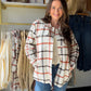 Model wearing an ivory and rust plaid shacket with a button front and chest pockets over a cream top and jeans.