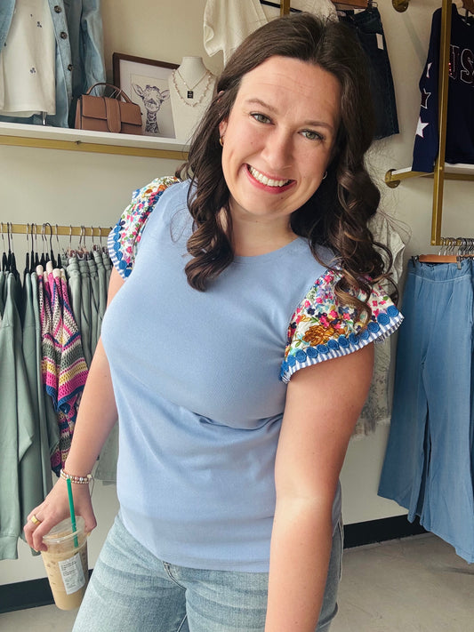Staccato

Elevate your everyday style with this Staccato mixed-media top featuring vibrant floral woven flutter sleeves and a soft ribbed knit body. The playful ruffled accents and delicate trim create a feminine, boho-chic silhouette that transitions perfectly from brunch to the office. It’s the ultimate combination of comfort and high-end detail for your spring-to-summer wardrobe.

Vibrant floral woven flutter sleeves.
Ultra-soft, breathable ribbed knit body.
Playful blue pom-pom trim detail.
Flattering, 