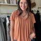 This Butter Orange Shirring Short Sleeve top features a flattering V-neck and short sleeves, designed with elegant shirring details for a refined silhouette. Its long length offers versatile styling options, making it suitable for both casual and polished looks. Crafted to combine comfort with a sophisticated touch, this top is an excellent addition to any wardrobe seeking effortless style.