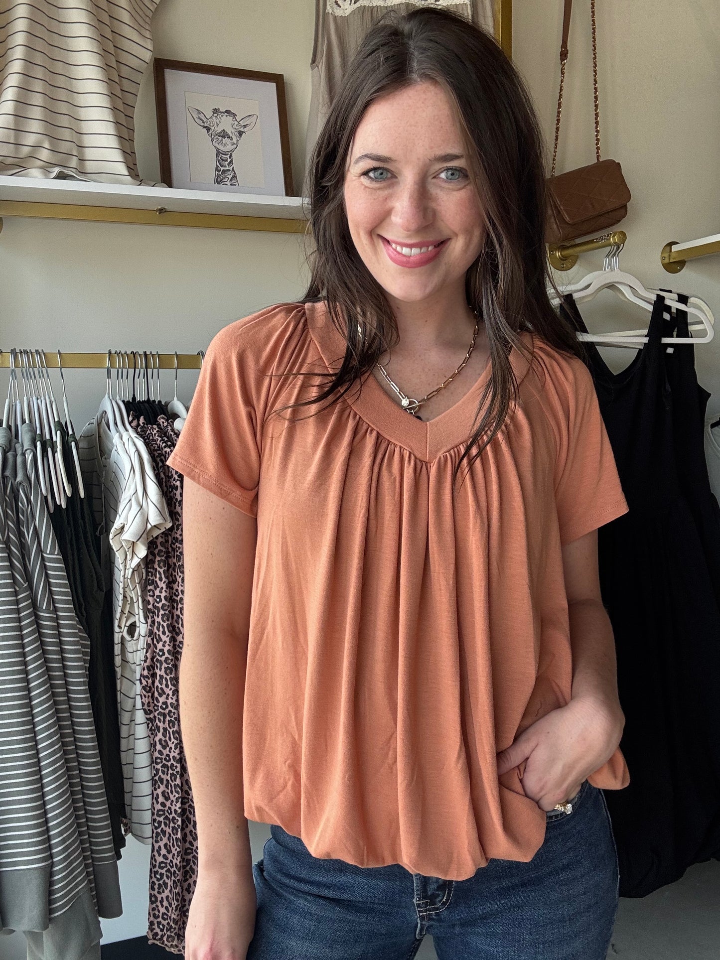This Butter Orange Shirring Short Sleeve top features a flattering V-neck and short sleeves, designed with elegant shirring details for a refined silhouette. Its long length offers versatile styling options, making it suitable for both casual and polished looks. Crafted to combine comfort with a sophisticated touch, this top is an excellent addition to any wardrobe seeking effortless style.