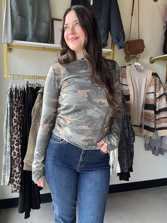 Add a fun twist to your wardrobe with this Camo Frilled Merrow Hem Top. The playful camouflage print pairs perfectly with the delicate frilled hem, adding a touch of flirty movement to your look. Featuring a cozy mock neck and long sleeves, this knit top keeps you comfy while standing out with style. Perfect for layering or wearing on its own, it’s a fresh way to mix casual with cute.