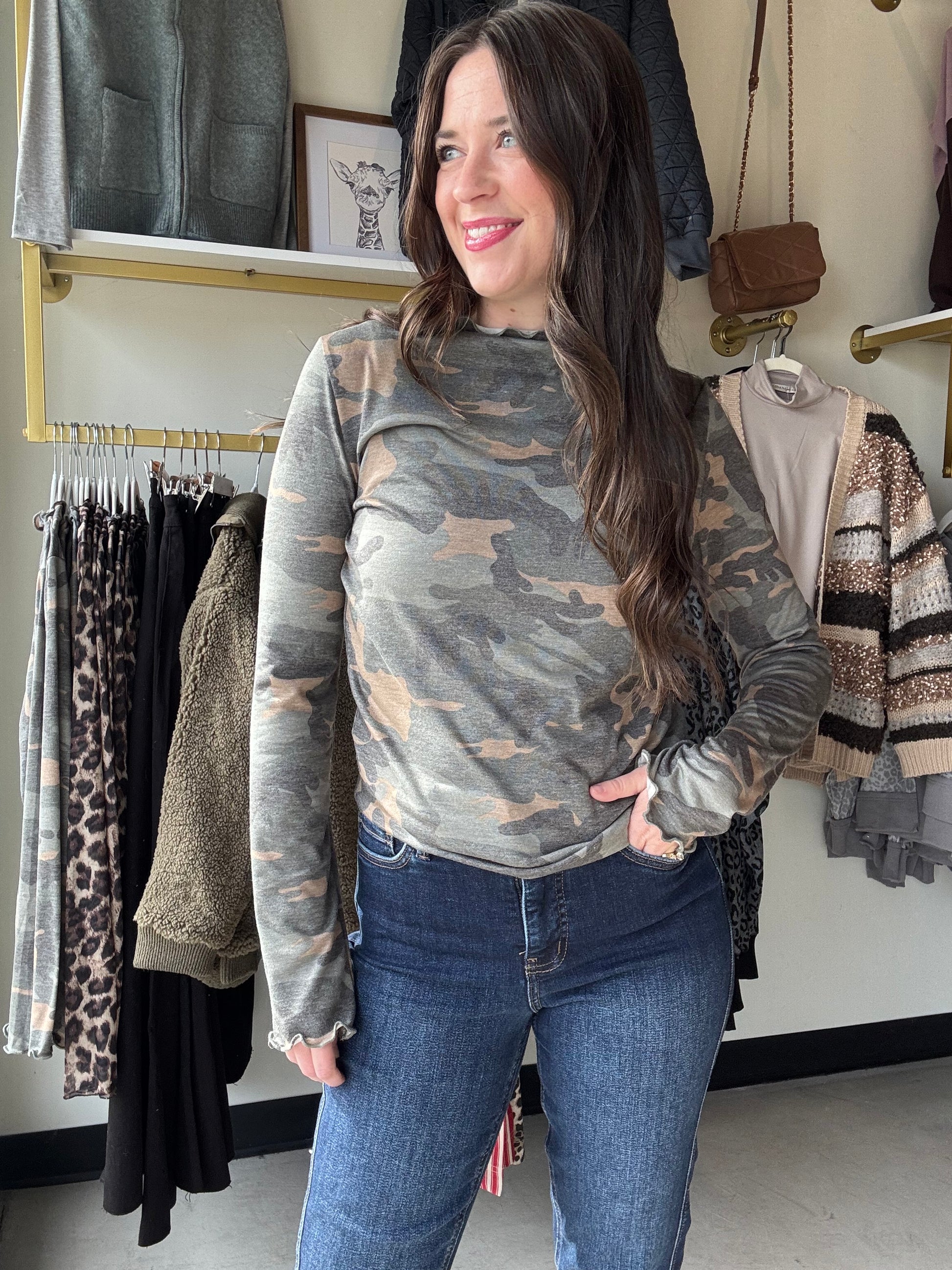 Add a fun twist to your wardrobe with this Camo Frilled Merrow Hem Top. The playful camouflage print pairs perfectly with the delicate frilled hem, adding a touch of flirty movement to your look. Featuring a cozy mock neck and long sleeves, this knit top keeps you comfy while standing out with style. Perfect for layering or wearing on its own, it’s a fresh way to mix casual with cute.