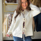 Model wearing an ivory knit cardigan with three bow-tie front closures over a floral top and jeans.