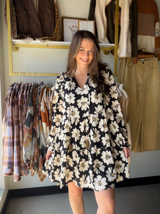 Turn heads in this dreamy floral mini from&nbsp;Doe &amp; Rae. A split V-neckline with tassel tie, long sleeves with ruffle trim, and a tiered skirt that moves beautifully — this dress does all the work for you. Wear it to brunch, a night out, or anywhere you want to feel effortlessly put-together.

Bold black &amp; white floral print with a feminine, editorial feel
Split V-neckline with tassel tie closure for a flirty, boho touch
Long sleeves with ruffle trim — elegant and season-spanning
Tiered mini skirt