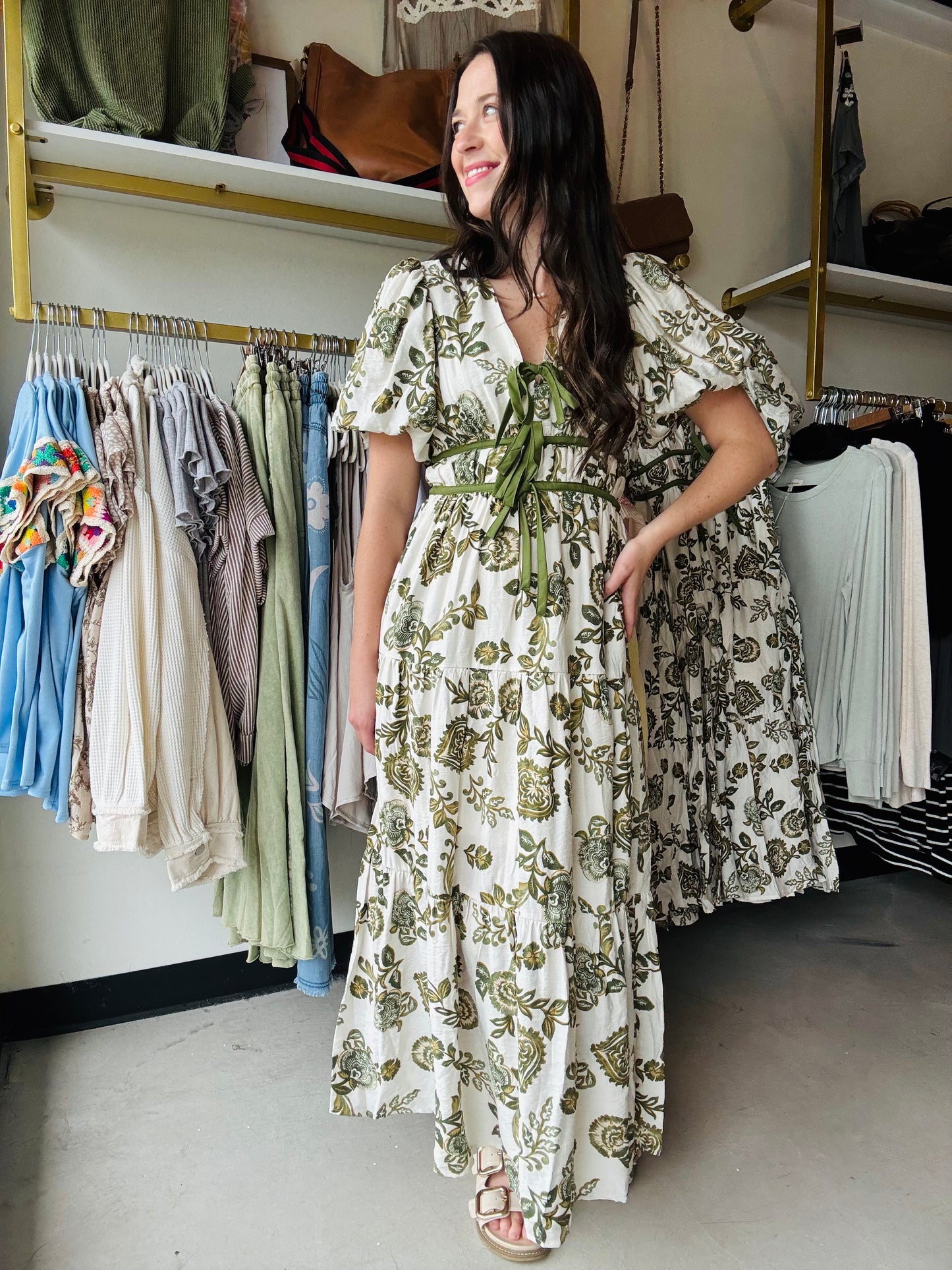 Entro

This Olive Floral Midi Dress combines elegance and comfort with its short bubble sleeves and flattering elasticated waist at the back. Crafted from lightweight woven fabric, it features a delicate floral print and a contrasting bow accent at the front for a refined touch. Fully lined and non-sheer, it offers modest coverage while side pockets add practical convenience. Ideal for stylish, effortless wear throughout the day.