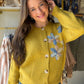 Some pieces just feel special. The&nbsp;Vintage Mustard Floral Button Cardigan by Rain &amp; Rose is one of them — a soft acrylic knit cardigan in rich vintage mustard, adorned with delicate floral appliqué along the front that makes it feel like a wearable heirloom. Classic button-front closure, relaxed silhouette, and feminine detailing that elevates everything from your favorite jeans to a flowy midi skirt.

Why You'll Love It

Delicate floral appliqué detailing — a feminine, one-of-a-kind statement piec