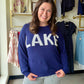 Jess Lea

Brighten your wardrobe with this breezy lightweight sweater in navy blue, featuring eye-catching white lettering that adds personality and charm. Perfect for layering on mild days or wearing solo when the weather's just right, this piece strikes the ideal balance between comfort and style. The playful color combo makes it a versatile go-to that pairs effortlessly with your favorite jeans, skirts, or casual bottoms. Lightweight enough for spring strolls and cozy enough for cool evenings—your new fa