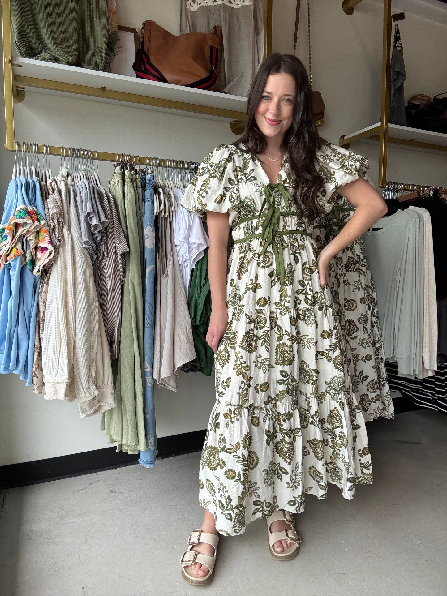 Entro

This Olive Floral Midi Dress combines elegance and comfort with its short bubble sleeves and flattering elasticated waist at the back. Crafted from lightweight woven fabric, it features a delicate floral print and a contrasting bow accent at the front for a refined touch. Fully lined and non-sheer, it offers modest coverage while side pockets add practical convenience. Ideal for stylish, effortless wear throughout the day.