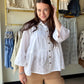 Effortlessly polished, endlessly wearable. The White Textured Tiered Top is crafted from 100% cotton in a soft tonal dot weave that adds subtle dimension without trying too hard.

A crisp pointed collar and full button-front closure give it a refined, put-together feel, while the shirred ruffled hem and gently gathered waist create natural volume and a flattering silhouette. Full-length sleeves and thoughtful seaming add structure — making this one of those tops that looks just as good tucked into wide-leg 