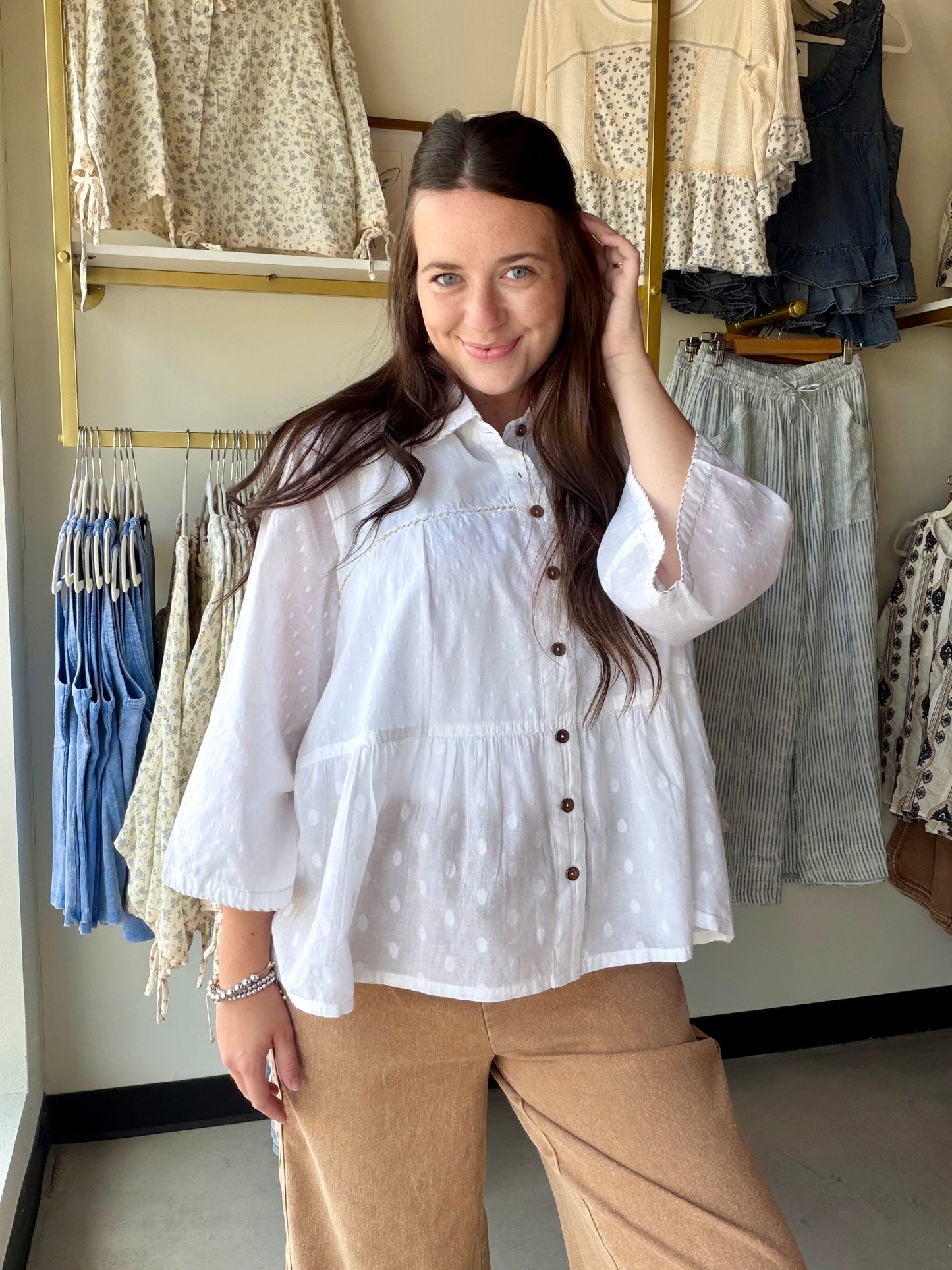 Effortlessly polished, endlessly wearable. The White Textured Tiered Top is crafted from 100% cotton in a soft tonal dot weave that adds subtle dimension without trying too hard.

A crisp pointed collar and full button-front closure give it a refined, put-together feel, while the shirred ruffled hem and gently gathered waist create natural volume and a flattering silhouette. Full-length sleeves and thoughtful seaming add structure — making this one of those tops that looks just as good tucked into wide-leg 