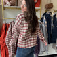 The Rust &amp; Mocha Plaid Jacket features a fully lined interior, ensuring comfort and durability throughout the season. Its boxy fit provides a modern silhouette while allowing ease of movement. Designed in rich fall tones of rust and mocha, this jacket effortlessly complements autumn wardrobes. Practical front pockets add functionality without compromising style, making it an essential outerwear piece for transitional weather.