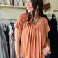 This Butter Orange Shirring Short Sleeve top features a flattering V-neck and short sleeves, designed with elegant shirring details for a refined silhouette. Its long length offers versatile styling options, making it suitable for both casual and polished looks. Crafted to combine comfort with a sophisticated touch, this top is an excellent addition to any wardrobe seeking effortless style.