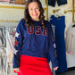 Ignite your patriotic spirit with this navy long-sleeve top featuring bold sequin "USA" lettering and embroidered star sleeves. Perfectly festive and effortlessly stylish, it’s the ultimate statement piece for every American celebration.